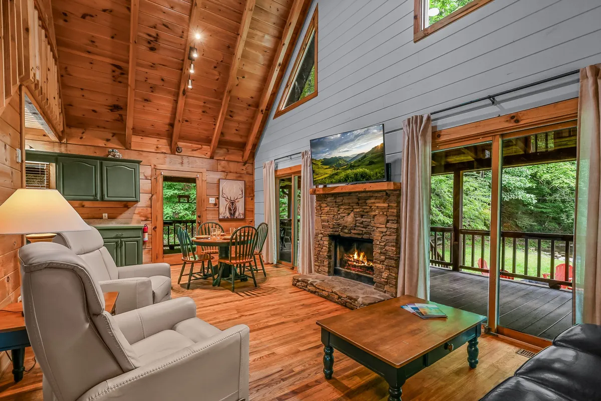 A warm and inviting living room featuring a prominent wood-burning fireplace, large windows that let in natural light, a dining table set for socializing, and plush, comfortable seating. The scene conveys a cozy atmosphere perfect for family gatherings, relaxing by the fire, and enjoying meals or game nights together.