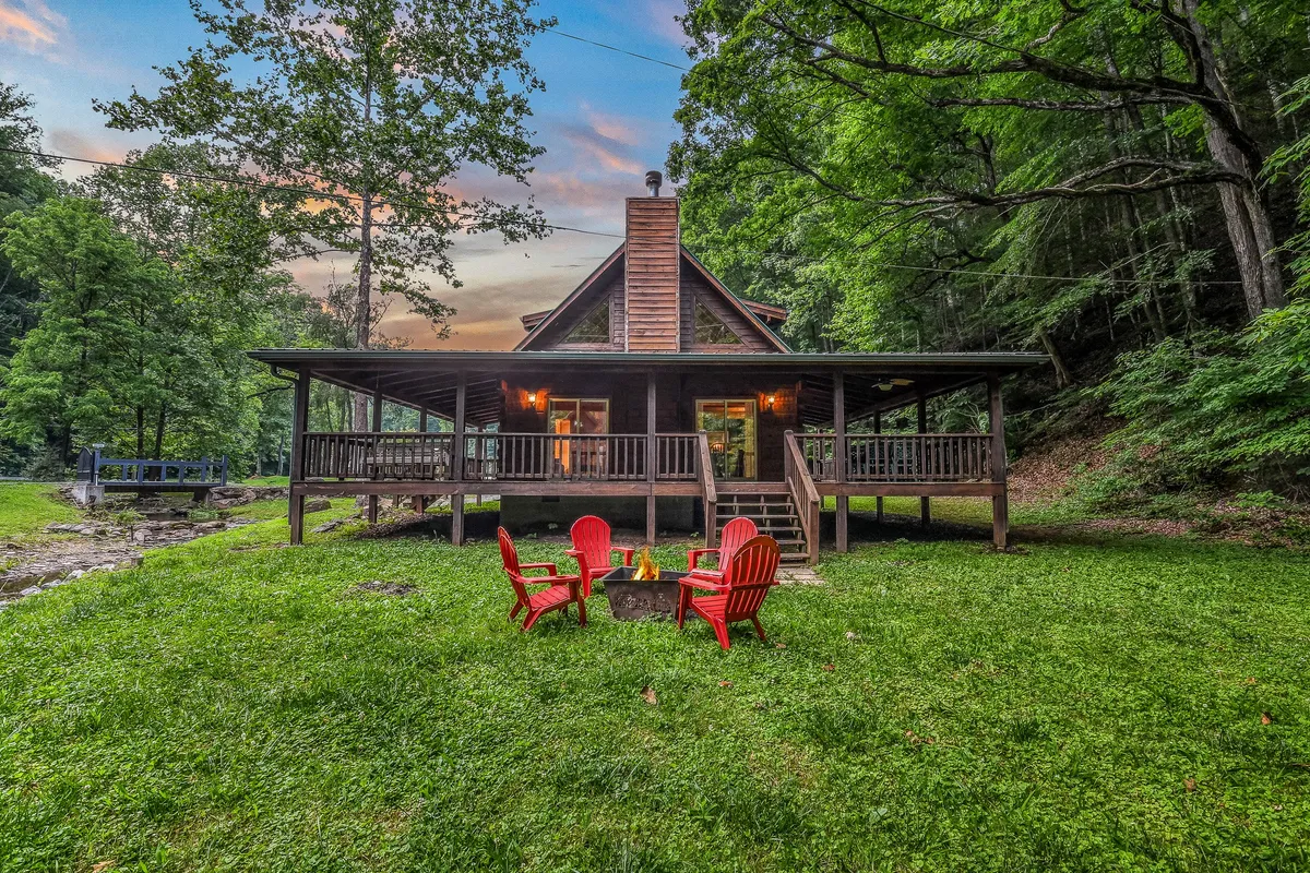 This exterior shot showcases the log cabin’s classic structure, with a focus on a set of red Adirondack chairs encircling a cozy fire pit, all nestled among tall trees. The inviting setup provides a perfect backdrop for evening gatherings, roasting marshmallows, or simply unwinding.