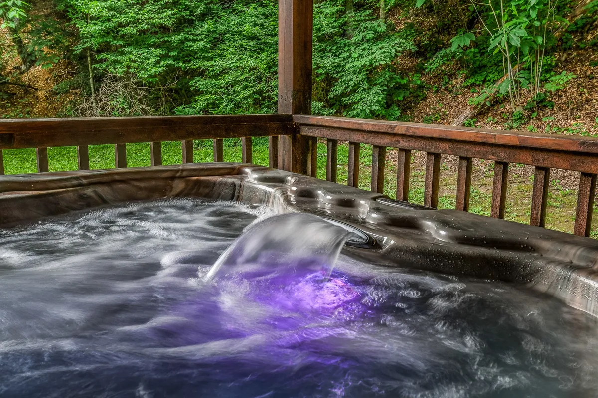 This image captures an inviting exterior setting featuring a hot tub overlooking a picturesque water feature surrounded by lush greenery. It conveys a tranquil space perfect for relaxation after a day of adventure, with the creek and natural landscape in full view.