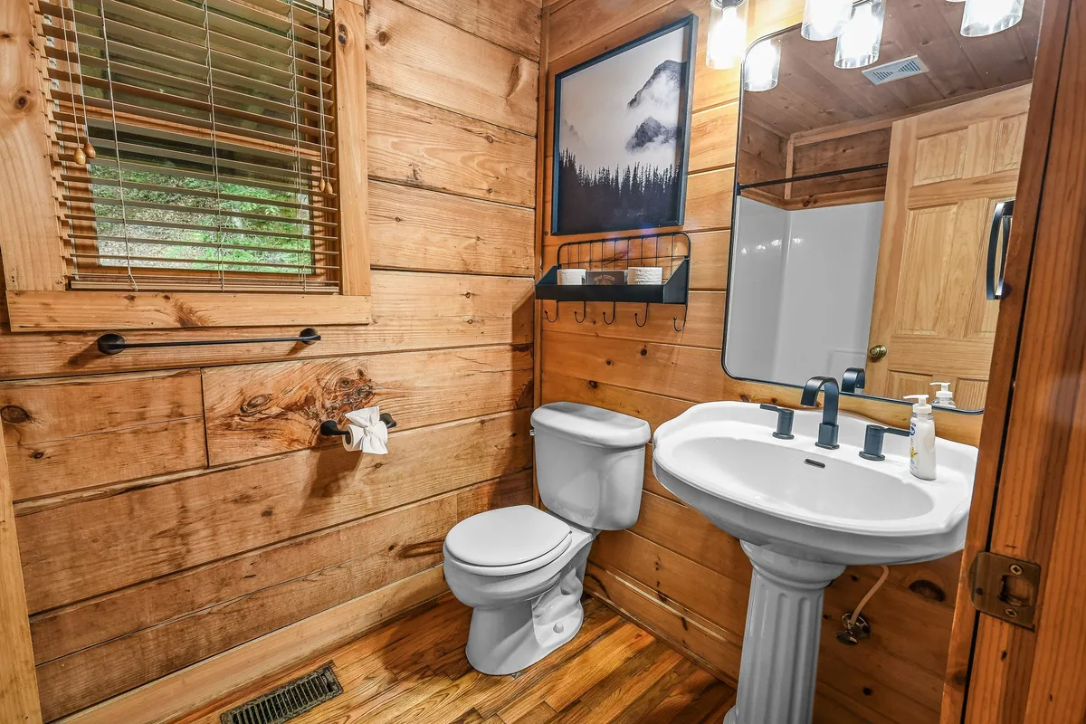 A charming, wood-paneled bathroom with a sink, mirror, and toilet. The décor features framed mountain photography and a welcoming, functional layout ideal for refreshing and starting the day.