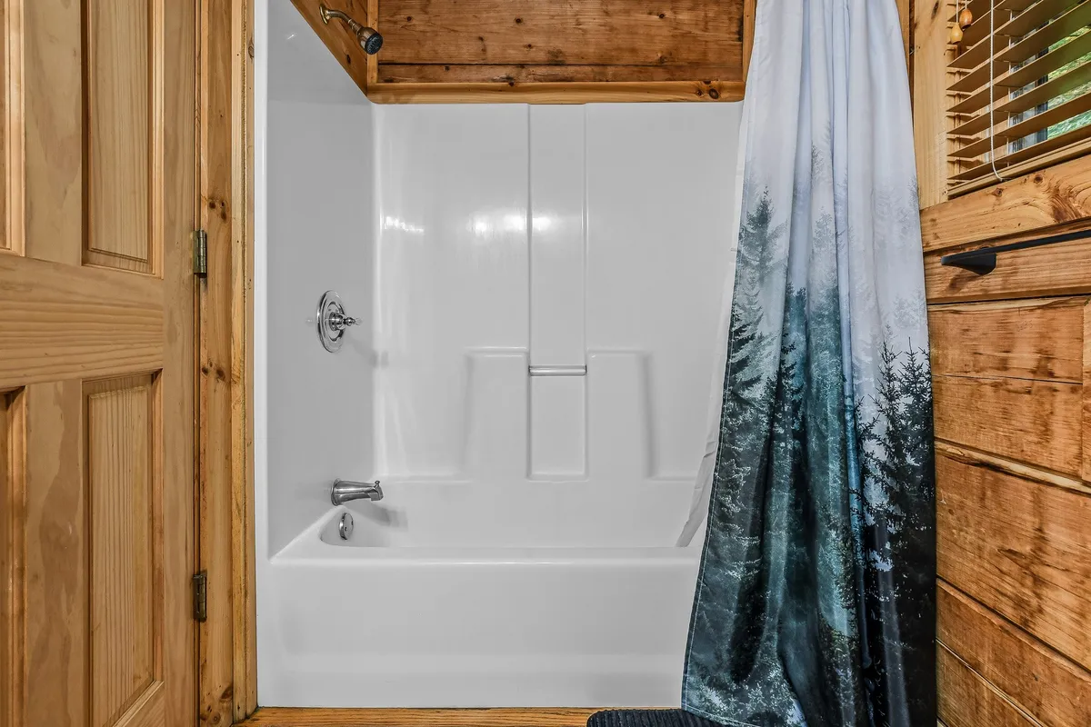 A bathroom with a bathtub and shower combo, surrounded by rustic wooden walls and a wooden door. The space feels tranquil and inviting, ideal for unwinding after a day of adventure.