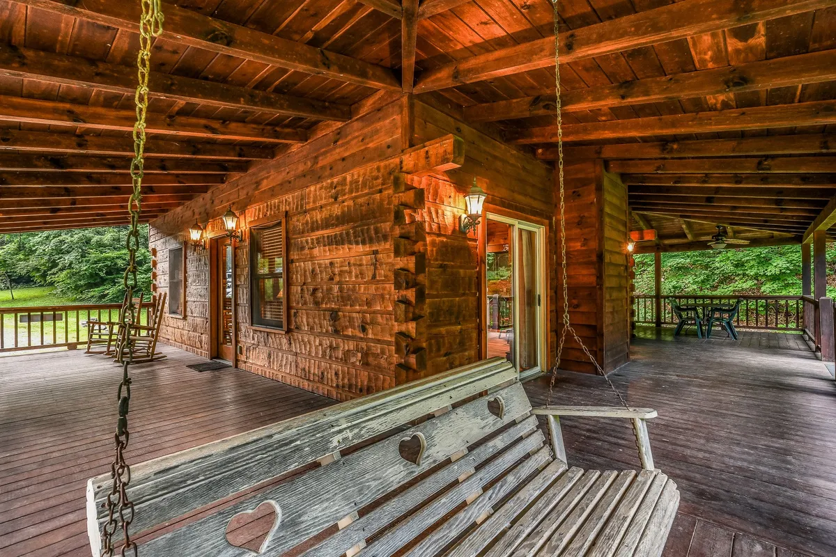 A charming wrap-around porch with a wooden swing bench and outdoor seating area, accented by lantern-style lighting and surrounded by natural beauty. The porch invites guests to relax with morning coffee, watch sunsets, or enjoy evening chats.