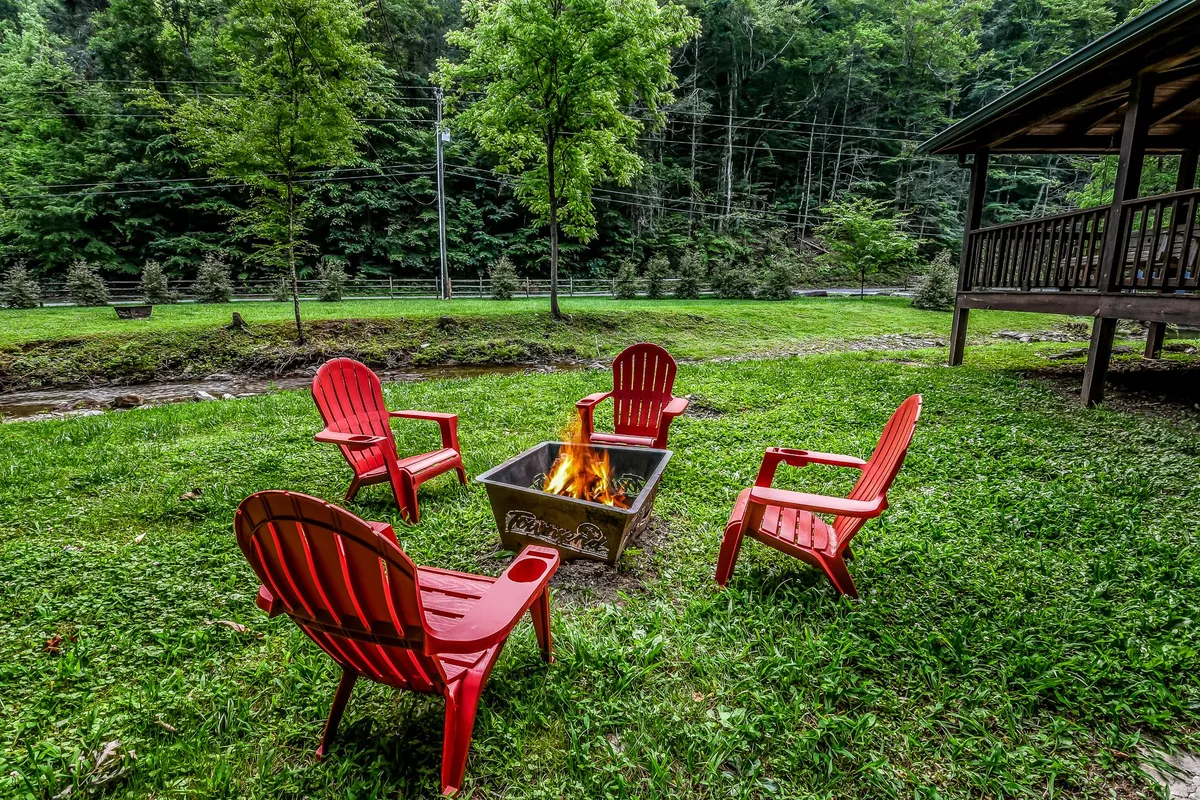 A cozy fire pit area with bright red chairs is set on a green lawn, bordered by trees. The inviting arrangement encourages guests to gather, share stories, and enjoy the outdoors under the stars—a natural extension of the adventure experience highlighted in the section.