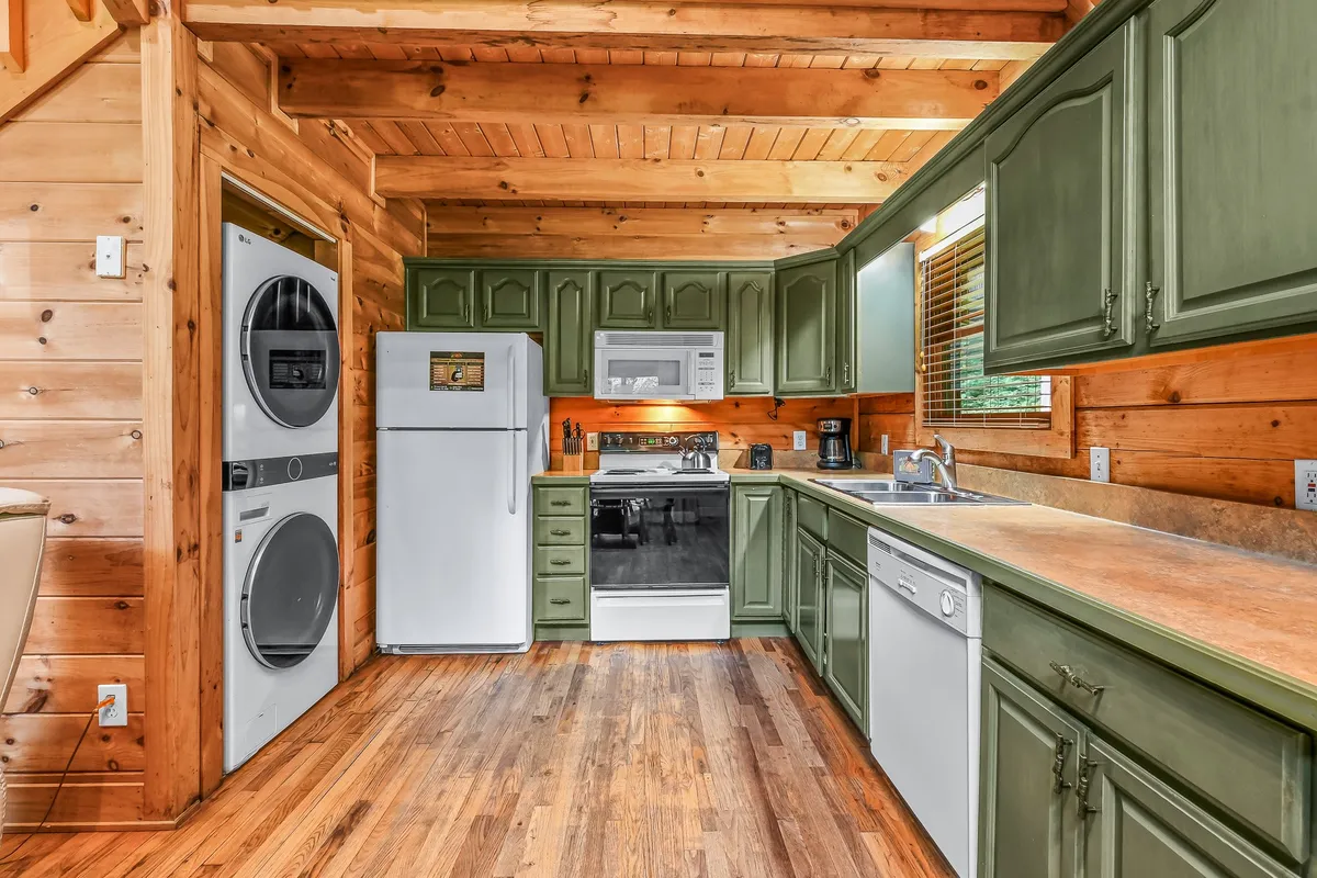 A close-up of the kitchen area, featuring green cabinetry, wooden countertops, and modern appliances. The layout is practical and stylish, with visible dish essentials and ample space for preparing family meals.